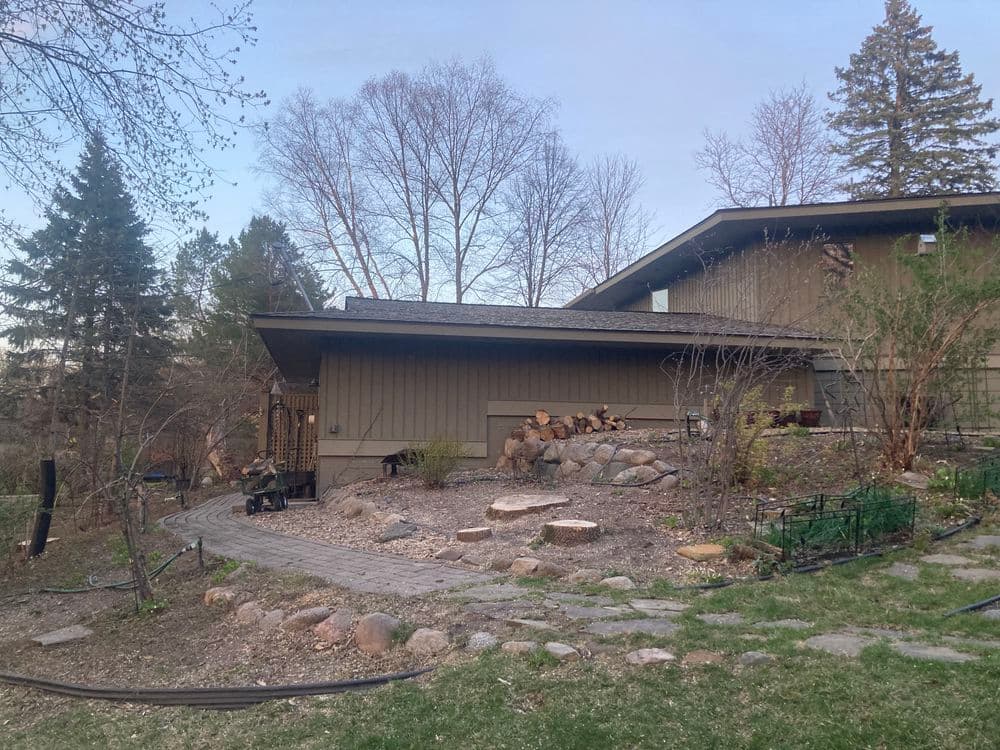 Modern home exterior surrounded by landscaped garden, stone path, and trees in the background.