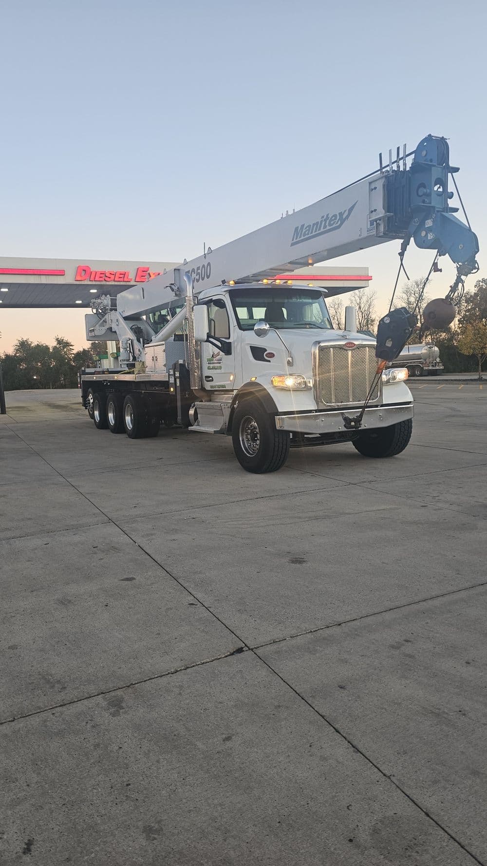 Mantey truck crane parked at a diesel fuel station, showcasing its extended boom and robust design.