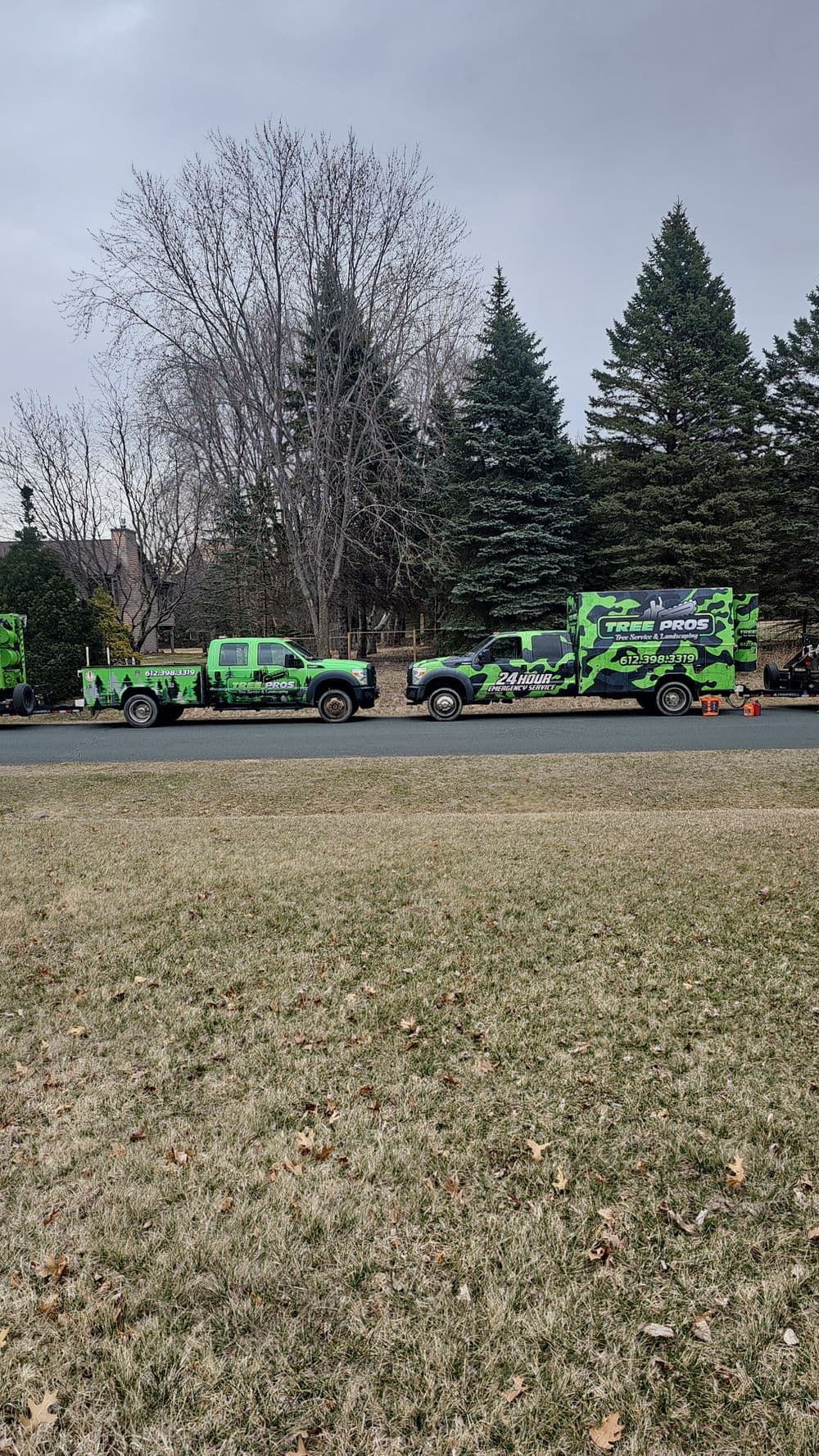 Green and black trucks parked on a residential street with trees in the background.
