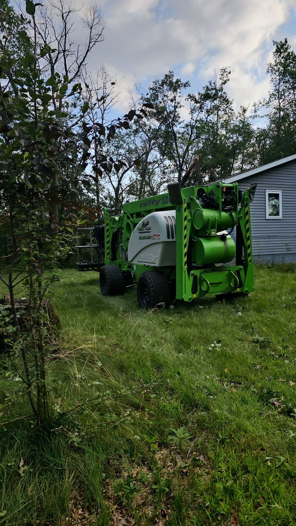 Green heavy-duty machinery parked on grassy area near a house in a wooded setting.