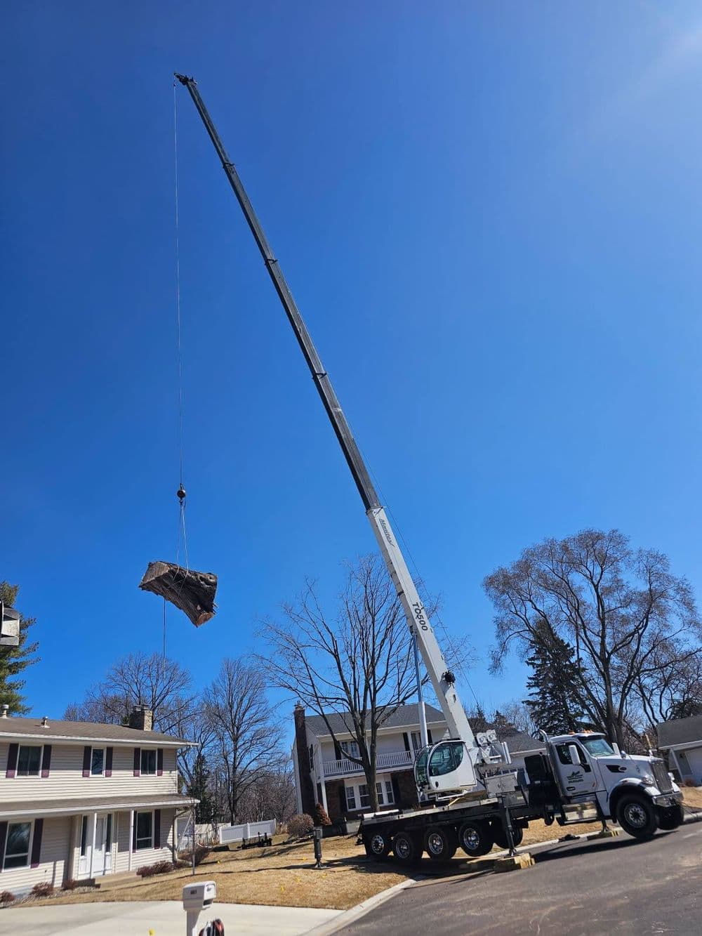 Crane lifting heavy object over residential area under clear blue sky.